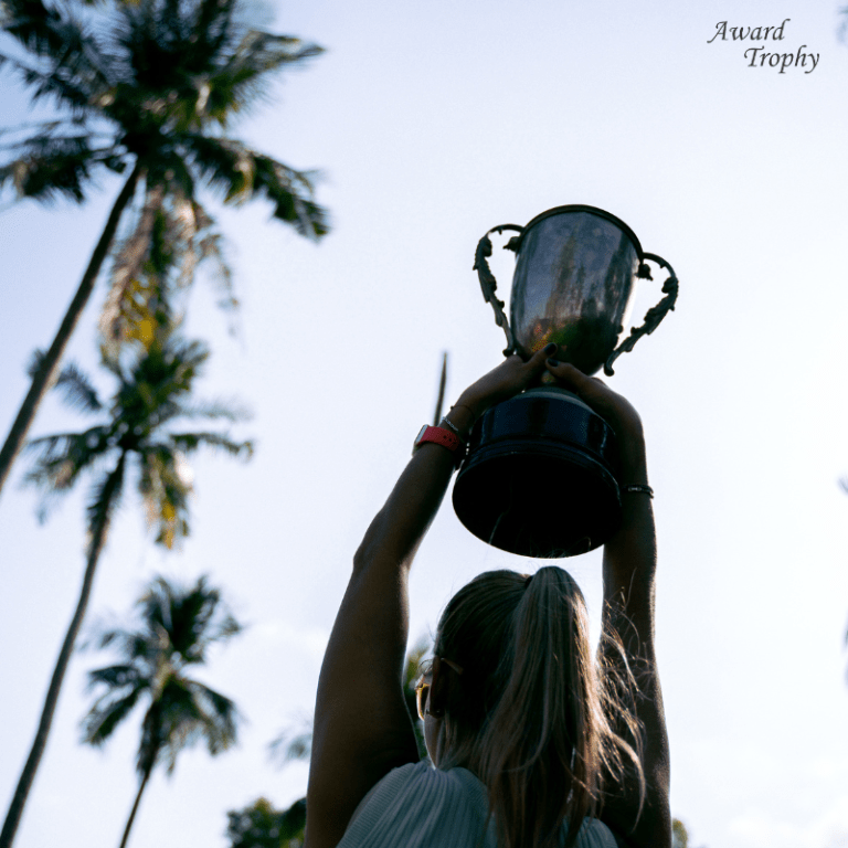 woman raising a trophy with palm trees in background